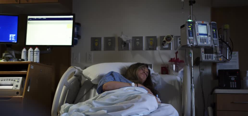 A female patient sleeping in a hospital bed surrounded by medical equipment