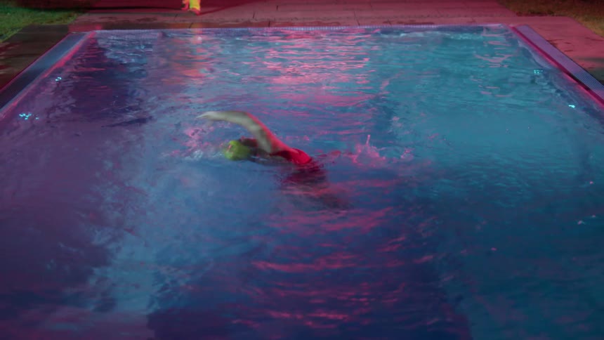 A woman does water aerobics in an in ground pool in the evening
