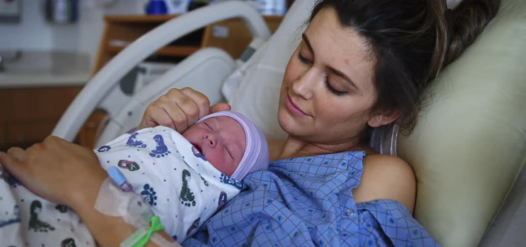 Woman lies in hospital bed holding blanket wrapped newborn