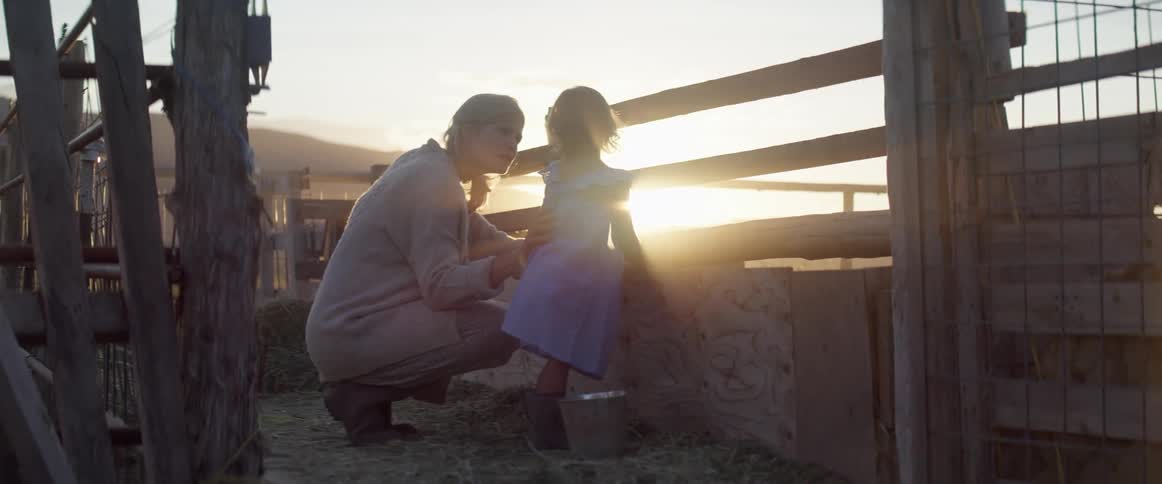 A woman stooping down and talking to a little girl in front of a fence
