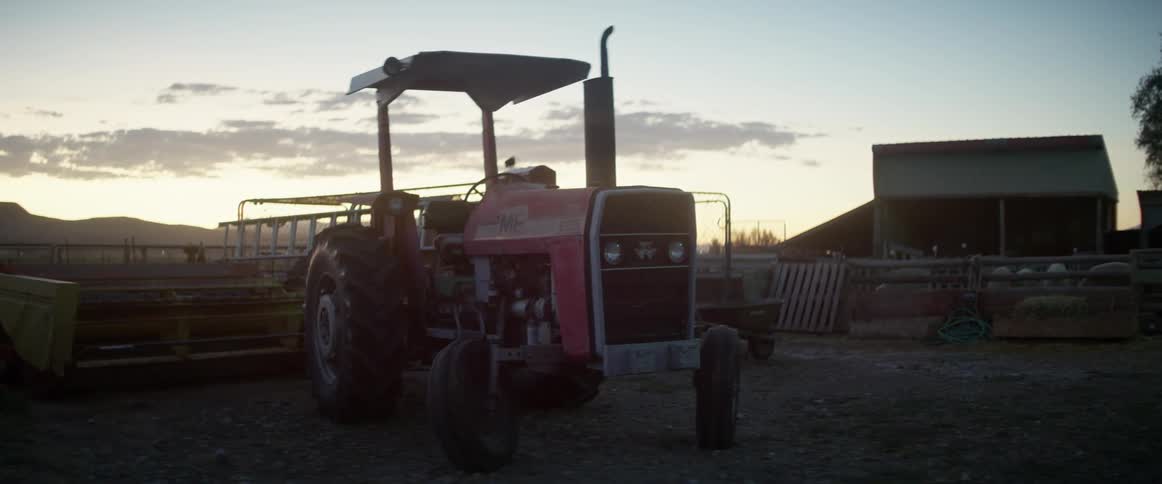 Red tractor sits near the fence on a farm at dusk