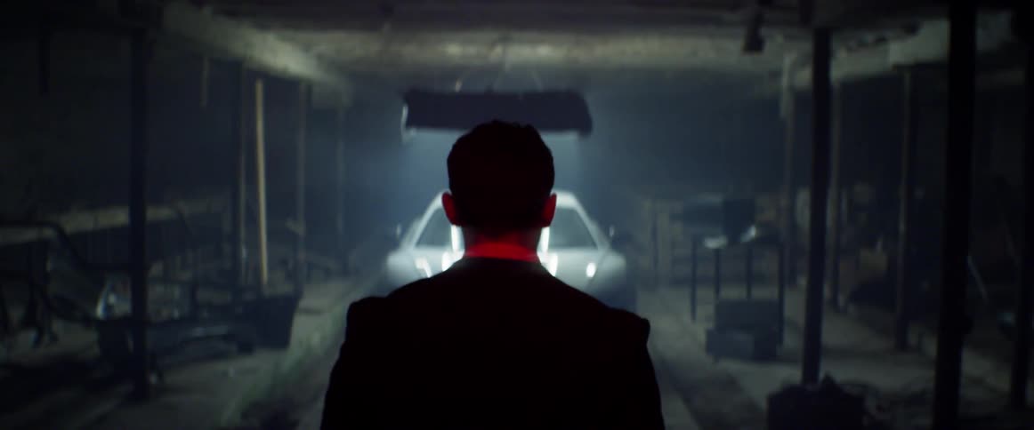 A man walks towards a sports car in a dimly lit garage
