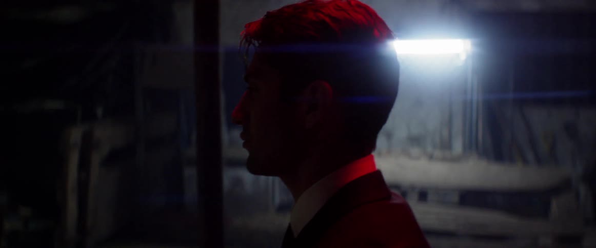 A man in a suit walks through a dimly lit garage