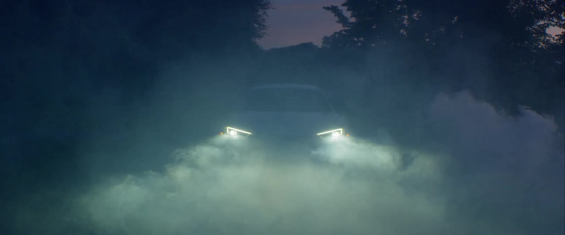A white sports car sitting on a road in fog flashes its lights on
