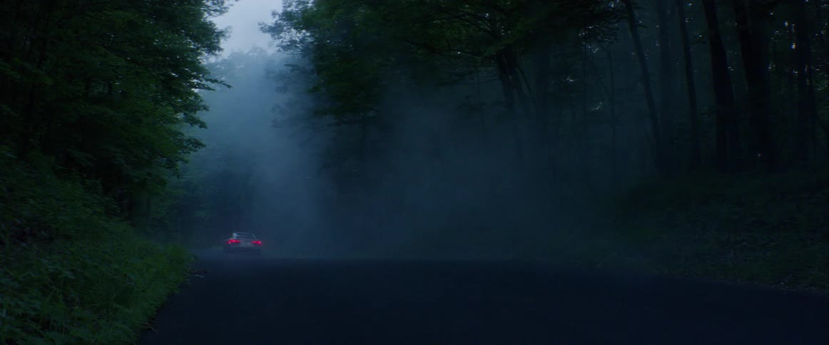A white car driving off into the distance around a curve