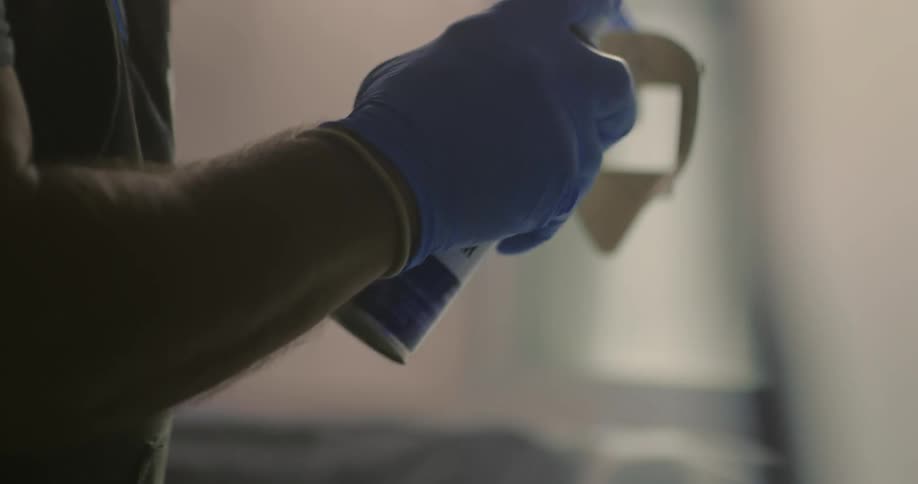 Man wearing protective gloves and mask sprays a piece of plastic