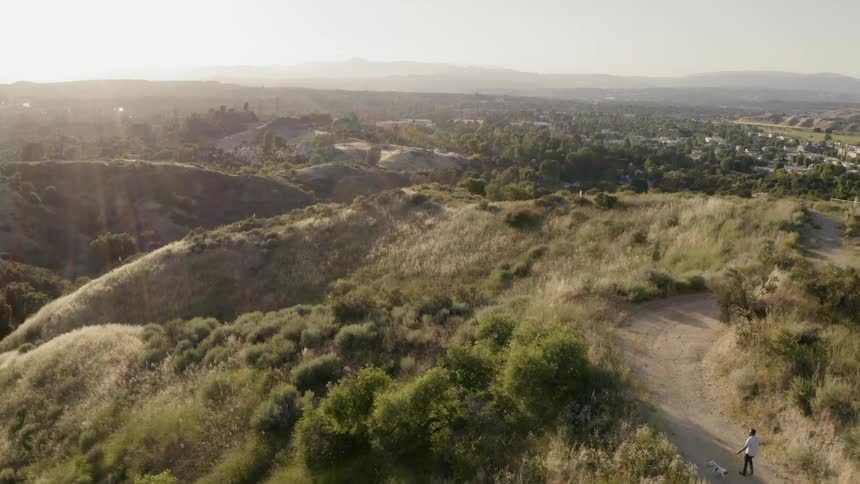 Aerial view of a man walking dog on dirt road in hills