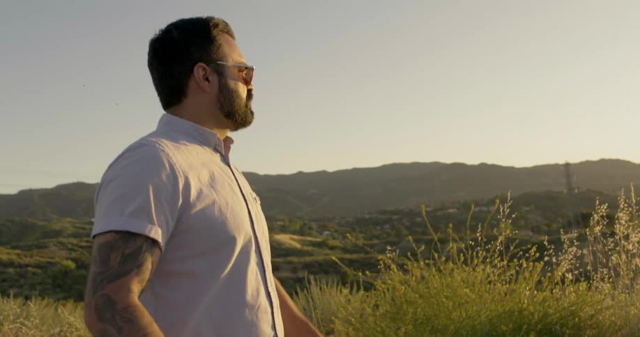 Man with beard and sunglasses walks on a hill at sunset