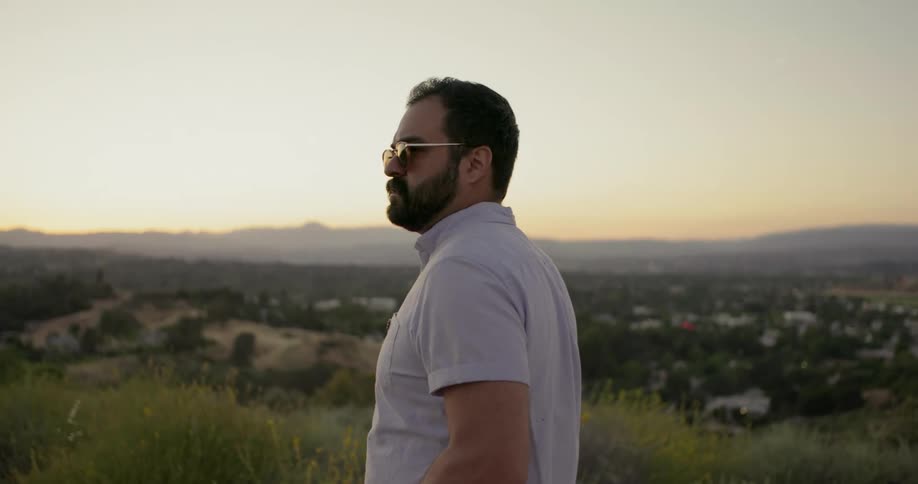 Man with beard and sunglasses walks on a hill at dusk