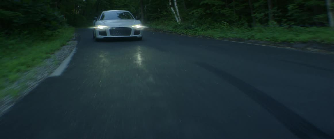 A white audi sports car driving on a road in a forest