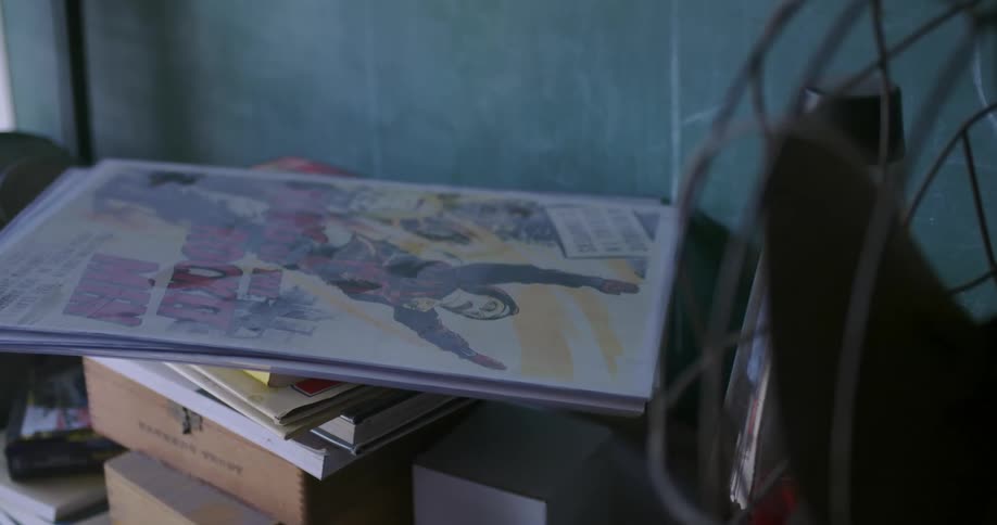 A movie poster sits on a pile of books and boxes net to a fan
