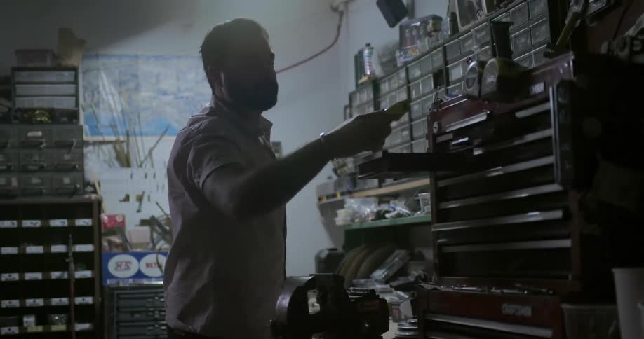 A man in a shop looks through a drawer and pulls out a part