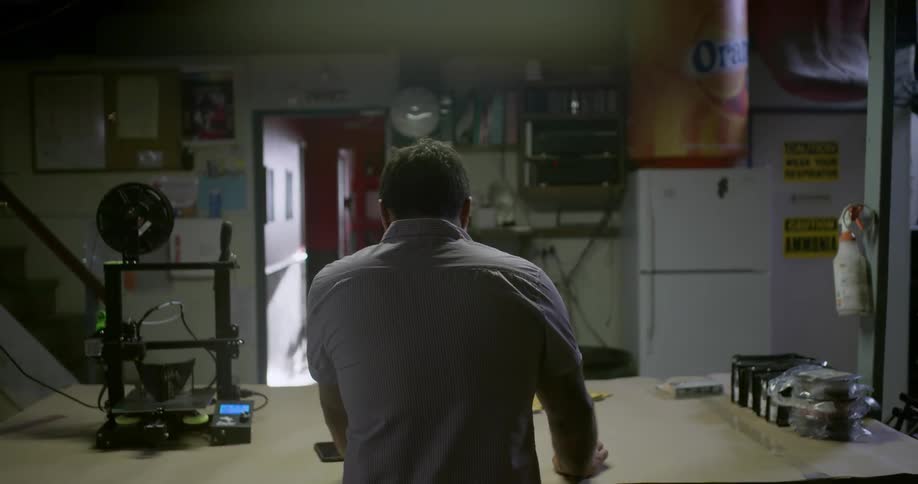 Man wearing a grey shirt stands and uses a laptop on a table