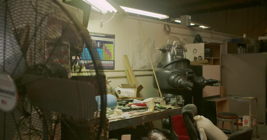 The lights turning on in a workshop room full of television props and various materials