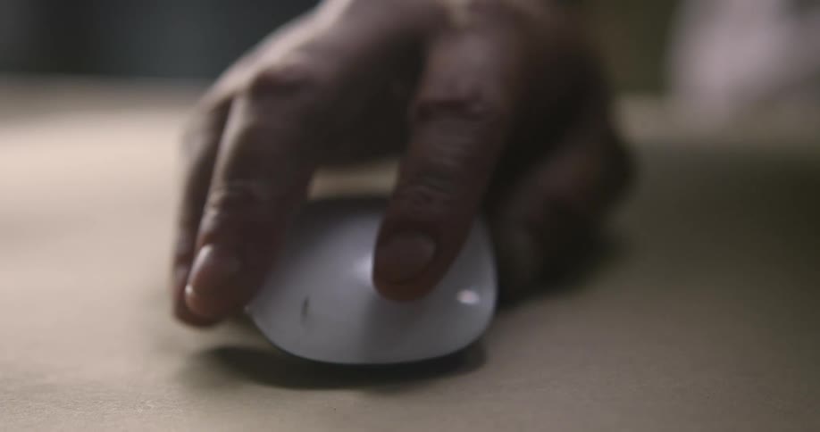 A white male slides a computer mouse forwards on a desk and clicks on it