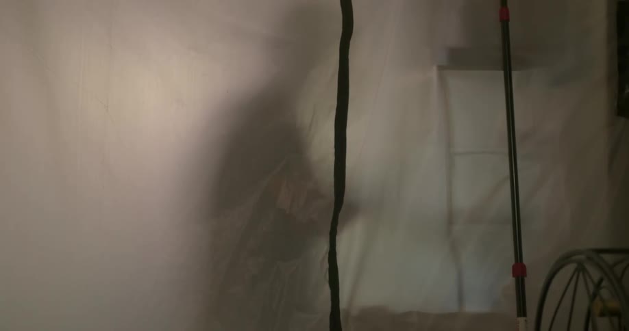 A man behind a translucent curtain hastily organizes items on a shelf in a medical facility