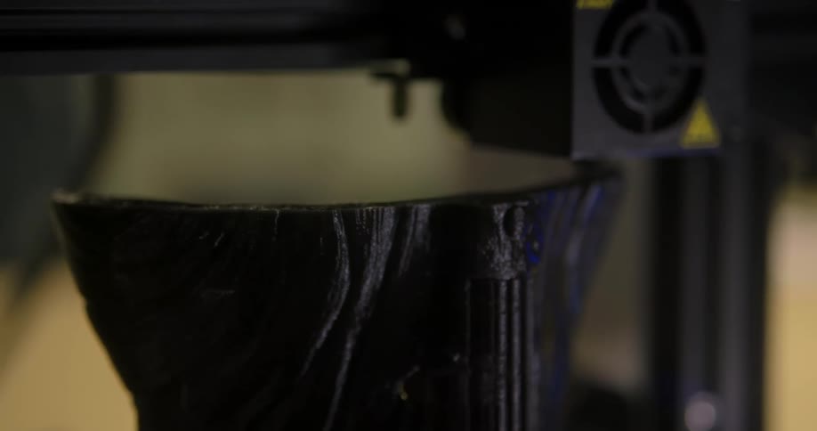 A 3d printer moves back and forth as it creates a tall black grooved object