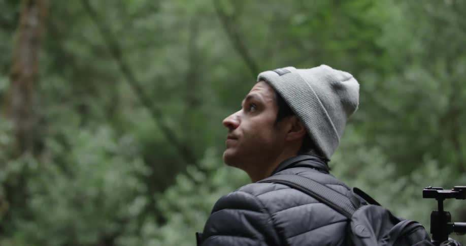 A man walks down a wooden pedestrian bridge in a forest as he looks up
