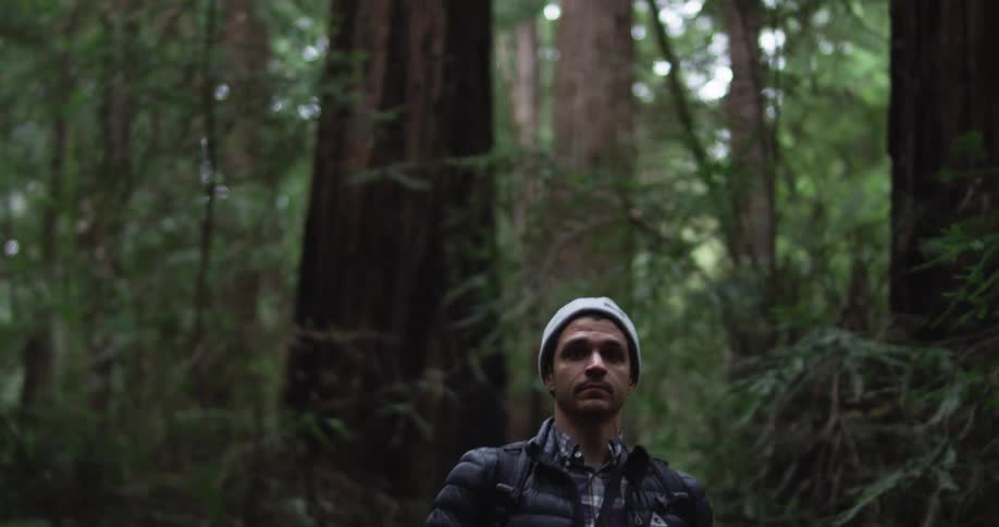 Man wearing a toque and jacket walks in the forest with a camera on a strap around his neck