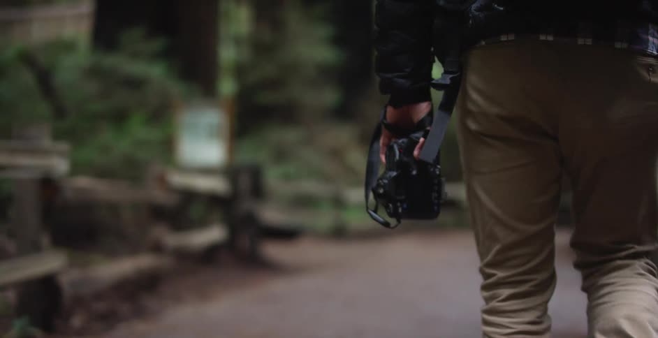 Male carrying a camera walks along a paved path through the woods in a nature center