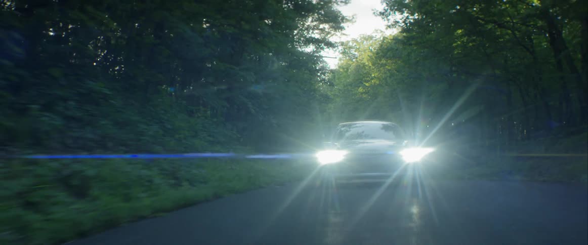 A white sports car driving down a two lane forested road
