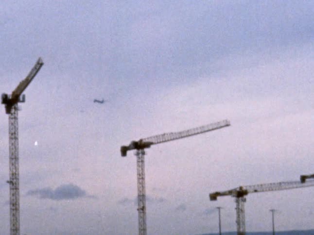 An airplane flies over large cranes