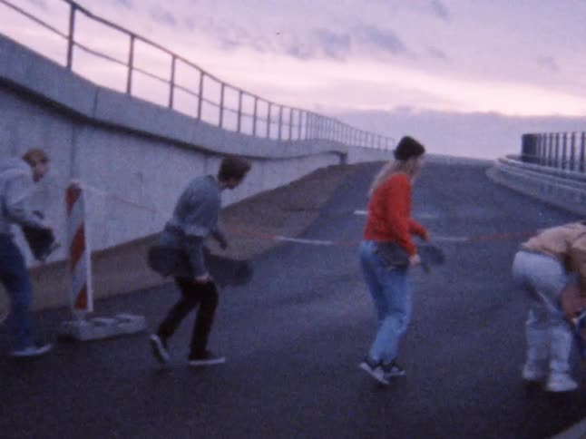 A group of skateboarders holding skateboards walk up the asphalt road