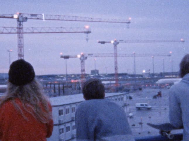 Four people overlooking an airport with airplanes and construction cranes