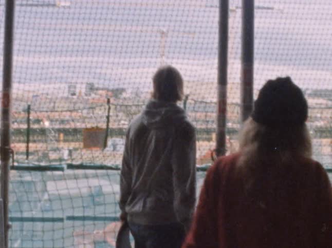 Three teenager with skateboards look through a fence at a construction zone