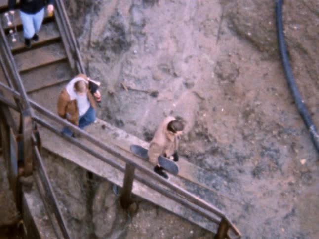 Three people walk down a flight off rocky and dirty mountain steps with skateboards