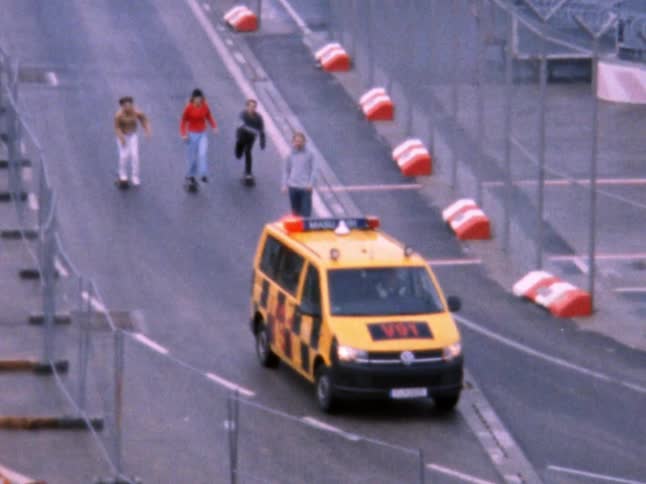 An emergency vehicle driving down a road with four people behind riding skateboards