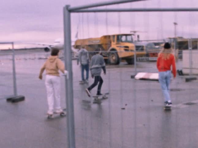 A small group of people skateboard through a parking area of a construction zone