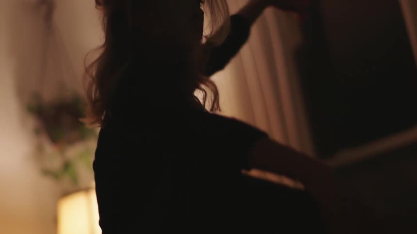 Woman practices dance moves in a room with a lamp turned on