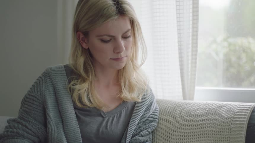 Blonde woman sitting on a couch on the living room of a house