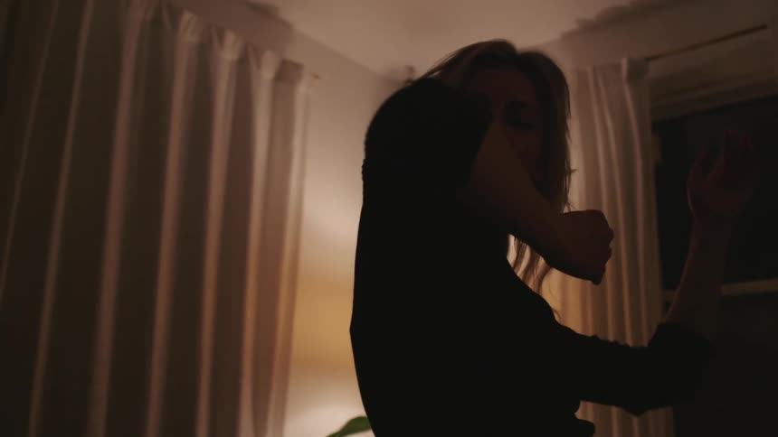 A woman moves her arms up and down and side to side as she dances in her living room