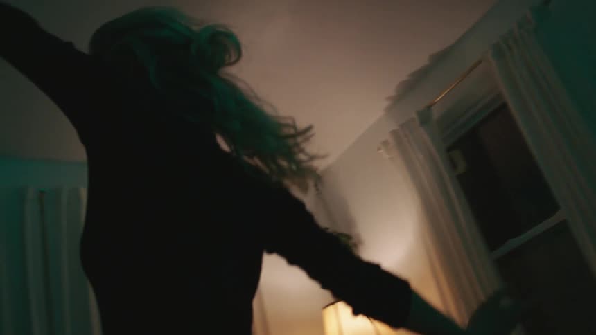 A woman dances around her living room at night