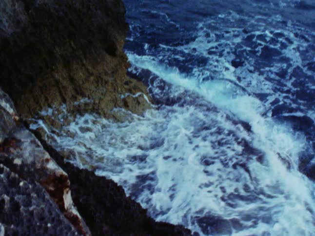 A foamy ocean wave hits a rocky coastline