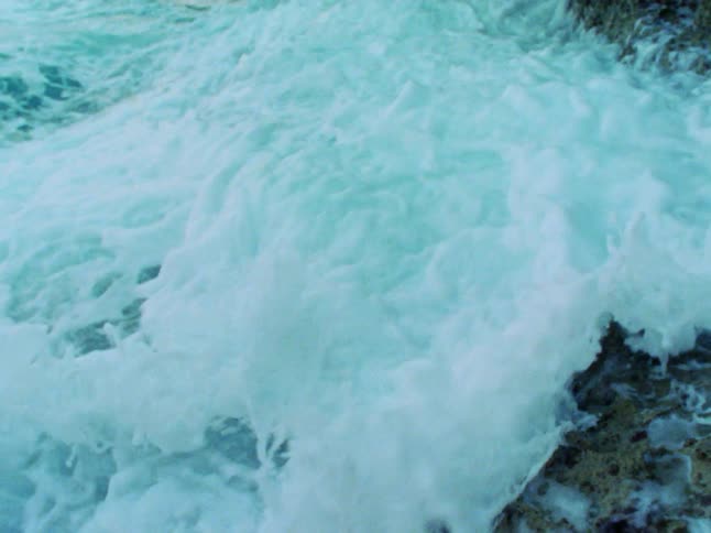 A foamy tidal waves rolls across a rocky shore