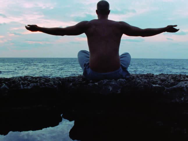 A man is meditating by the ocean