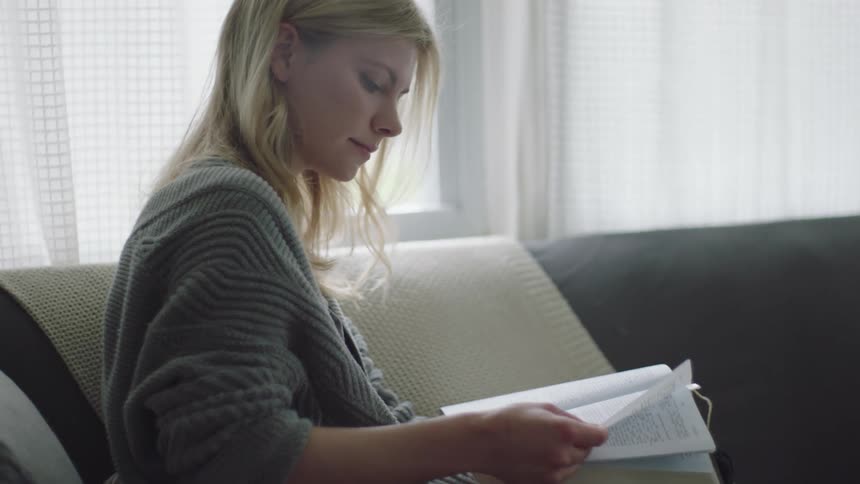 A white woman sits on a couch and reads a book