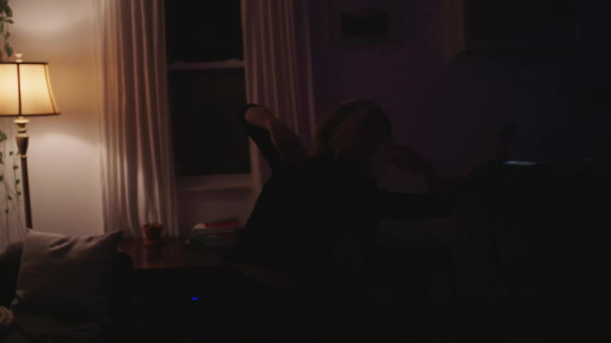 A white woman stretches her arms and bends backwards in her living room