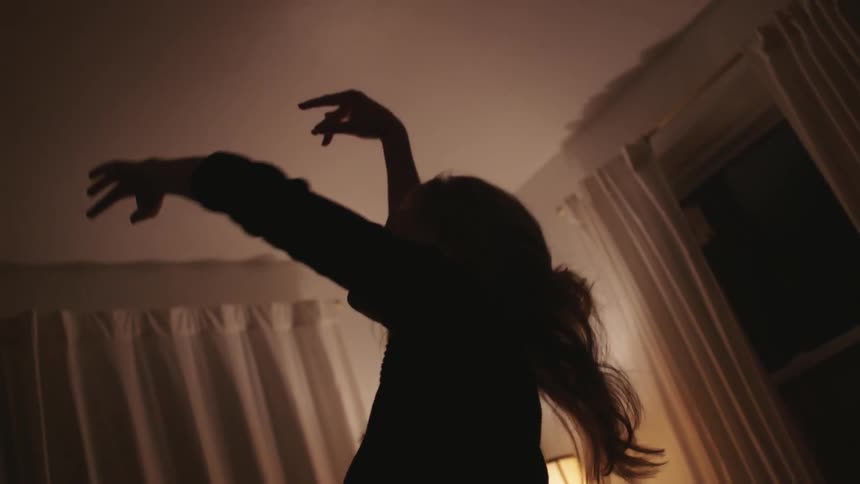 Woman with black sweater and blonde hair dances slowly in a room