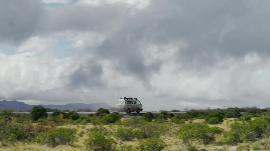 A van drives down a road that runs by a mountain