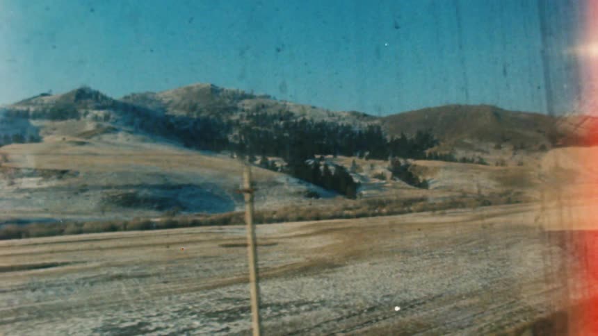 Train travels past the land and mountains under a sunny blue sky
