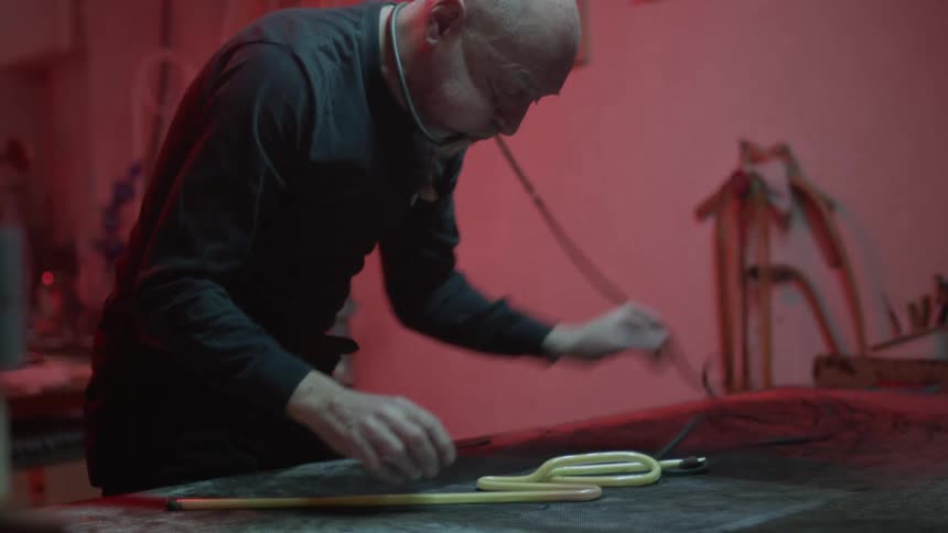 An elderly white man works with a yellow tube and a hand tool on a table