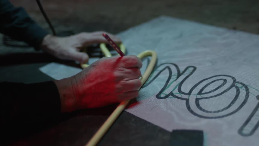 Person traces flowing script shapes onto paper using tube and pencil