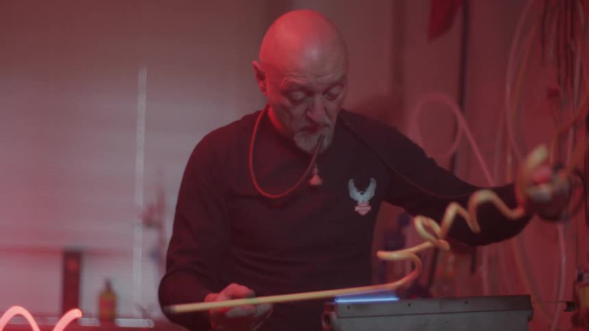 A white man turns a yellow tube over a flame in a workshop