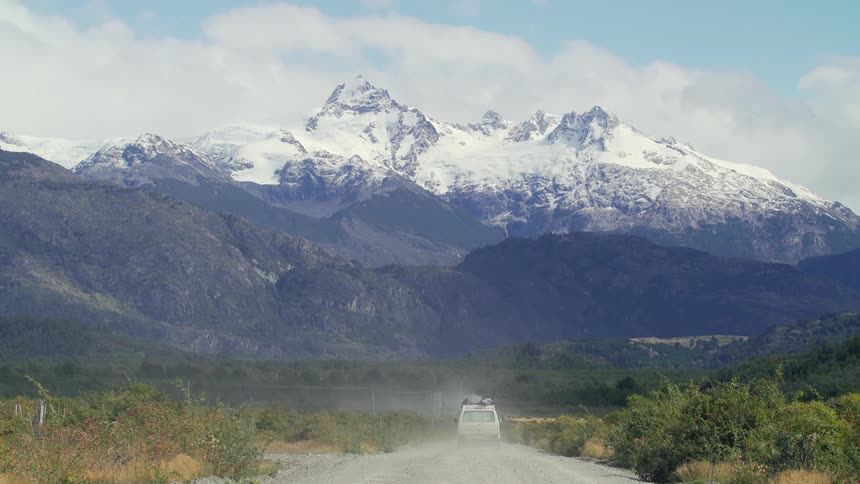 A white van drives down a gravel road head toward a mountain range