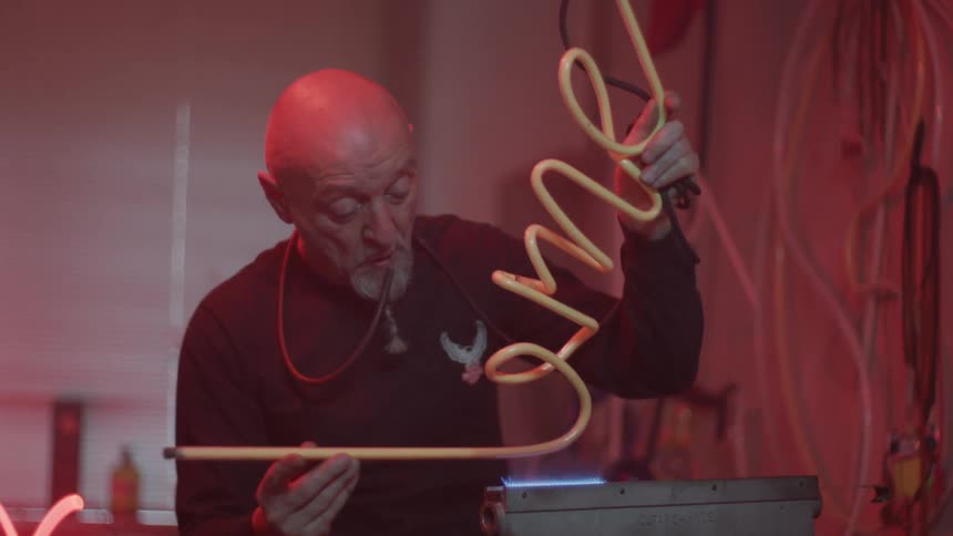 A white man works heating up a yellow snake tube with a blue flame