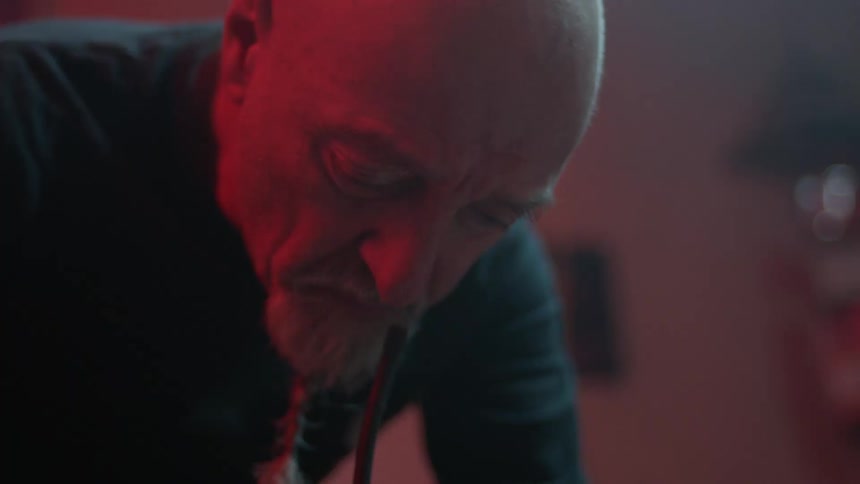 An old man with beard and bald head bends over in a room